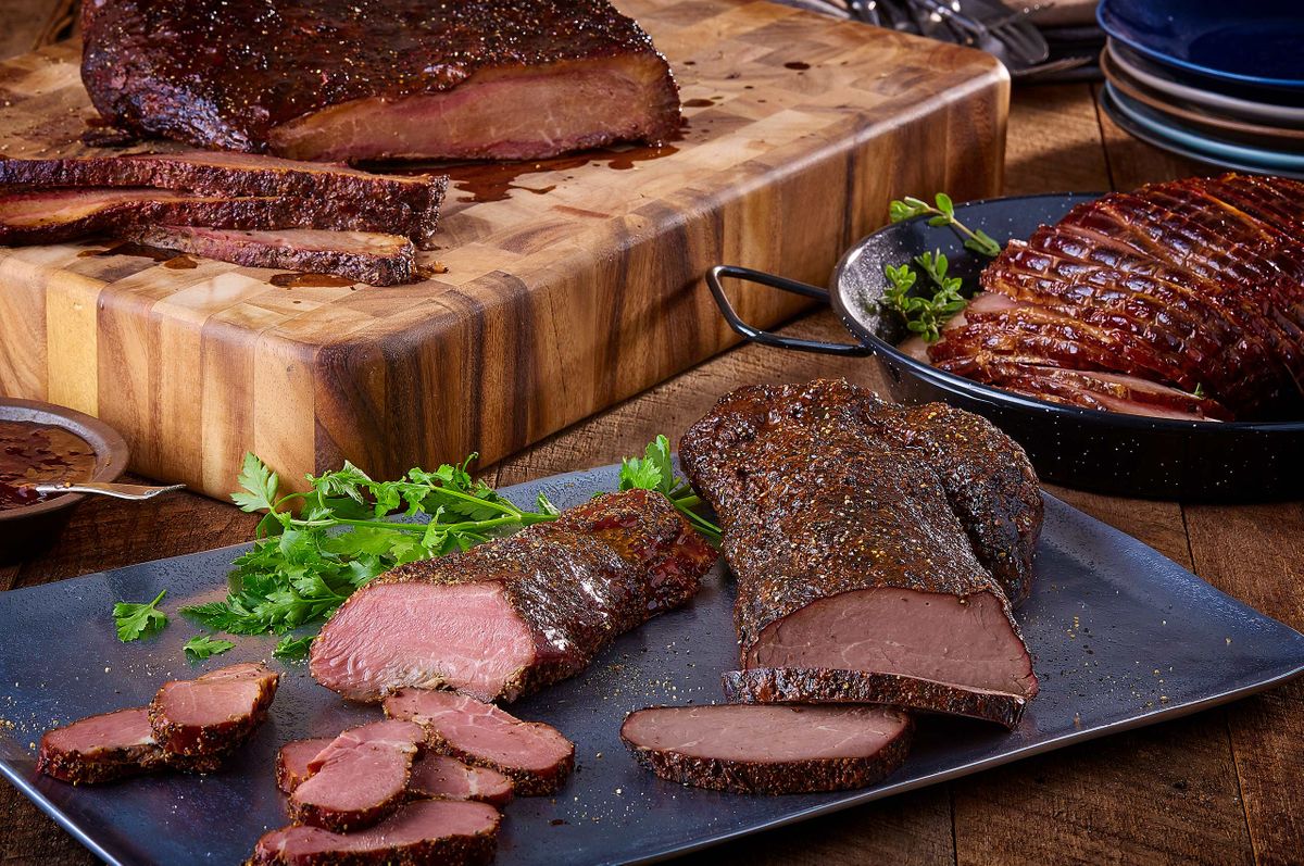 Ranch House Mesquite Smoked Meats table spread with peppered smoked beef, brisket on a butcher block, and glazed ham