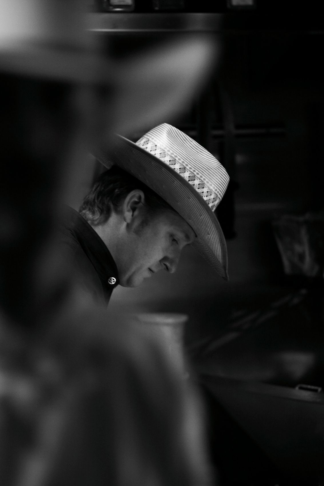 Black and white portrait of Chef Tim Love in a straw cowboy hat working head down in the Lonesome Dove kitchen