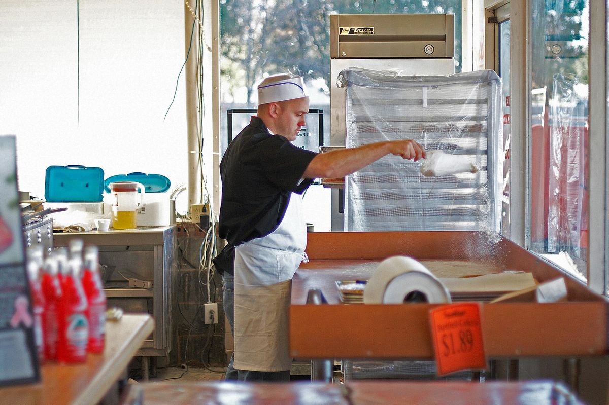 Cook dusting flour across a prep table in the open kitchen at Smokey's, cooling racks and dining room beyond