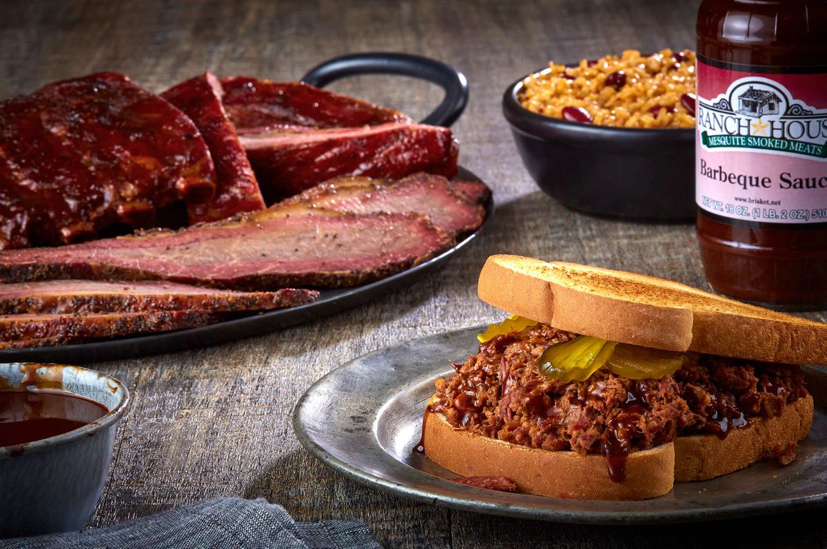 Ranch House Mesquite Smoked Meats chopped beef sandwich with pickles, beans, ribs, and the house Barbeque Sauce bottle