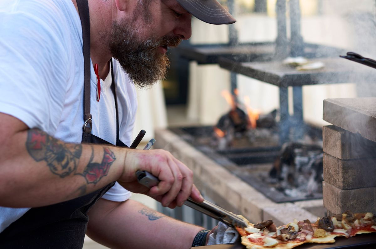 Chef Brent Hammer working a flatbread with mushrooms and cheese beside an open hearth fire