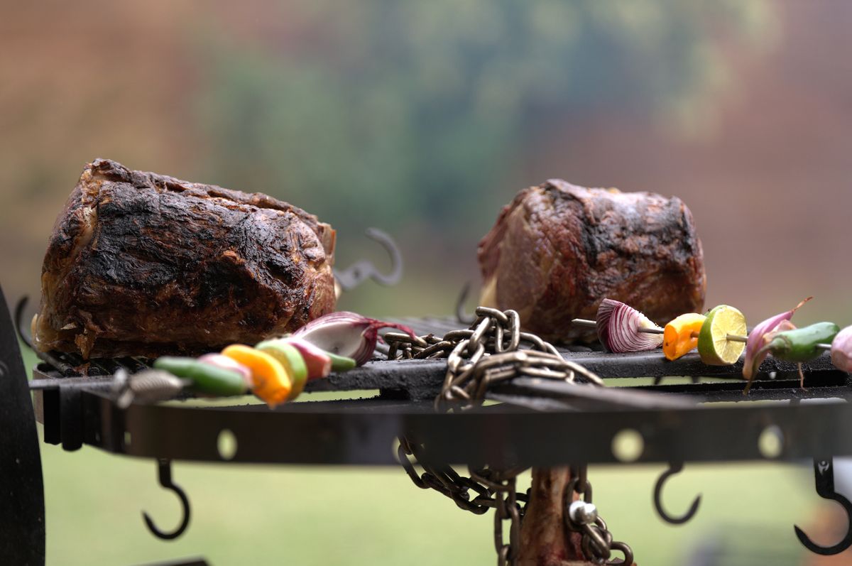 Two seared Rosewood Wagyu roasts resting on an iron grate beside pepper and onion skewers at an open-air asado
