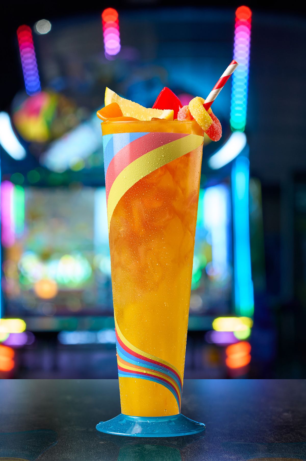 Bright orange fruit punch in a tall rainbow-swirl glass with pineapple and gummy-candy garnish at Malibu Jack's, by a DFW food and beverage photographer