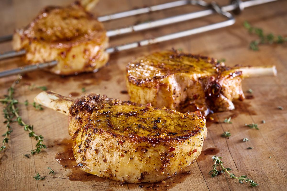 Fogo de Chão bone-in pork chops seasoned and seared on churrasco skewers over a wood board