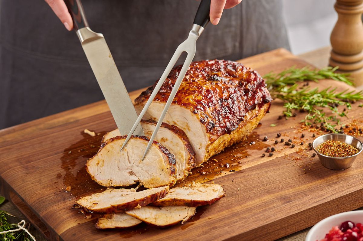 Carving a glazed roast at Fogo de Chão with knife and fork, rosemary, peppercorns, and spice rub alongside