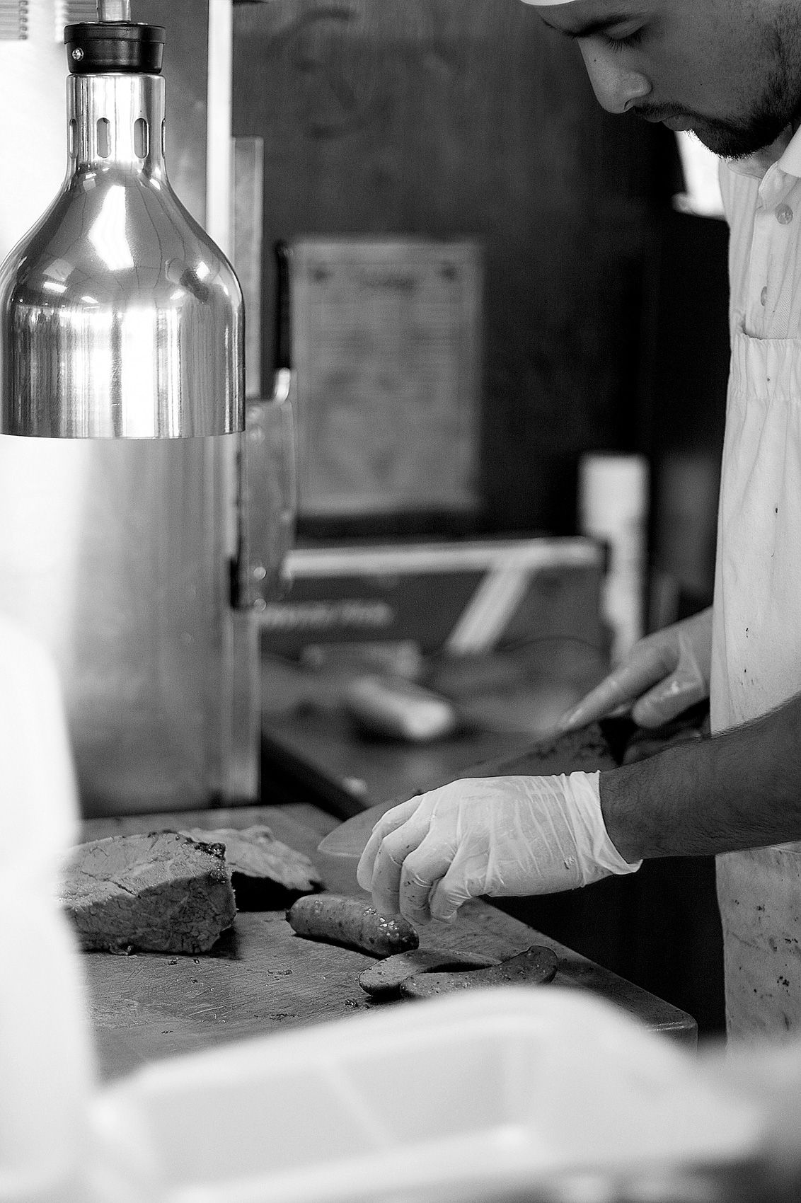 Gloved hands slicing brisket and sausage links on the cutting board under a heat lamp at Smokey's