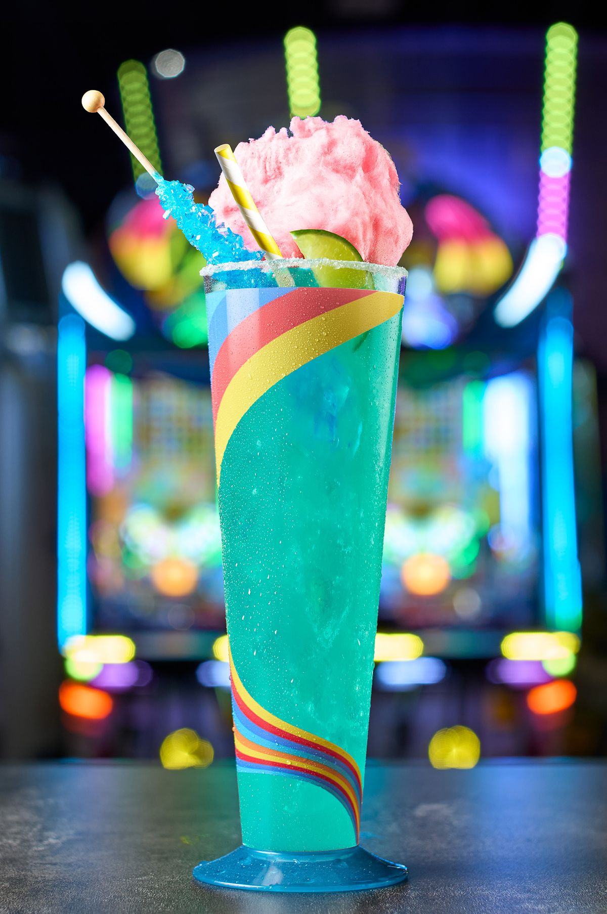 Teal novelty drink topped with cotton candy, a rock candy stick, and lime in a rainbow-swirl glass at Malibu Jack's, by a Dallas–Fort Worth drink photographer