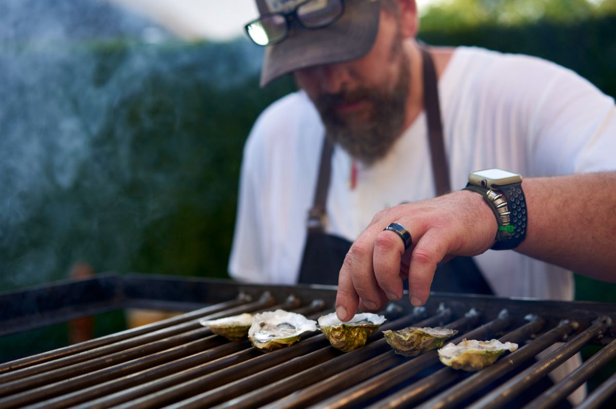 Chef Brent Hammer setting oysters on the half shell across a live fire grill grate