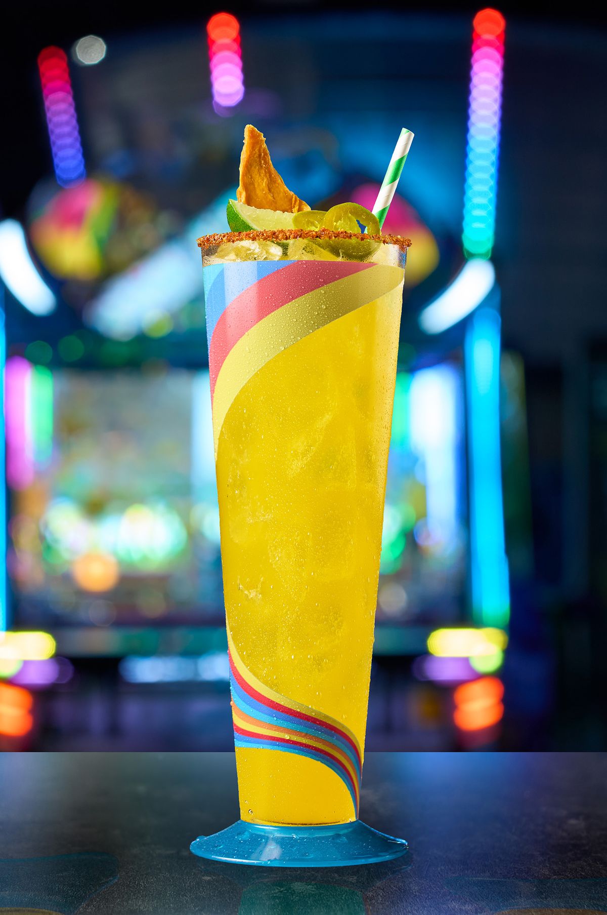 Bright yellow spicy margarita with a chili rim and jalapeño at Malibu Jack's, set against neon arcade lights, by a DFW beverage photographer