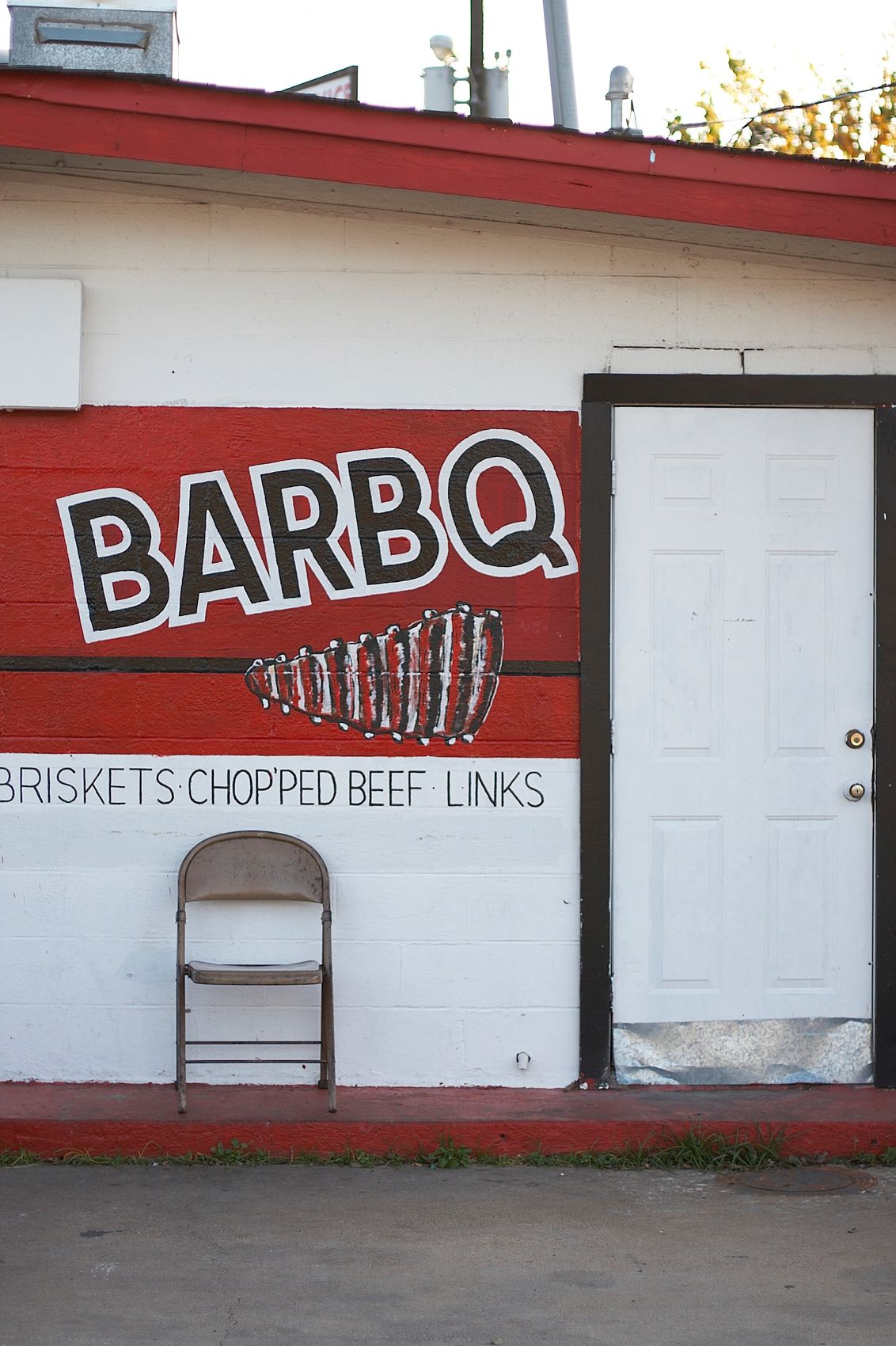 Hand-painted BARBQ sign advertising briskets, chopped beef, and links on the block wall at Meshack's in Garland, Texas