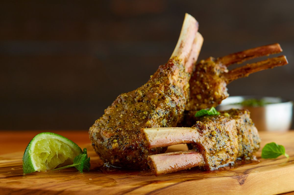 Fogo de Chão seasoned lamb chops stacked on a wood board with charred lime and fresh mint