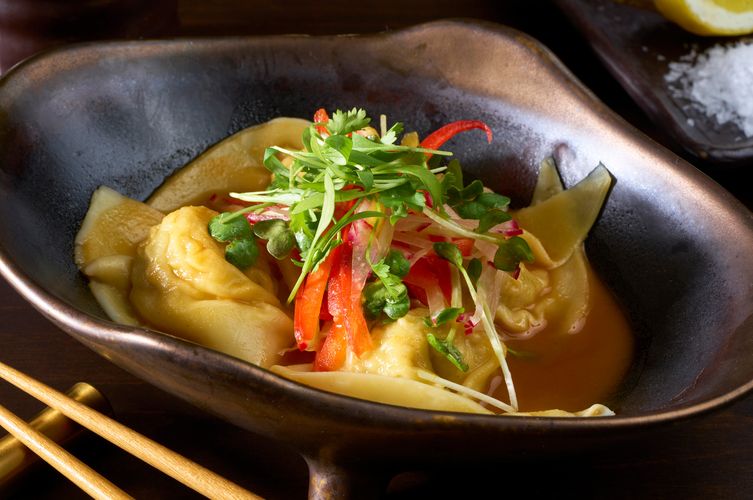 Dumplings in broth topped with red chili, radish, and microgreens in a dark ceramic bowl at Soy Cowboy in Arlington, by a DFW restaurant photographer