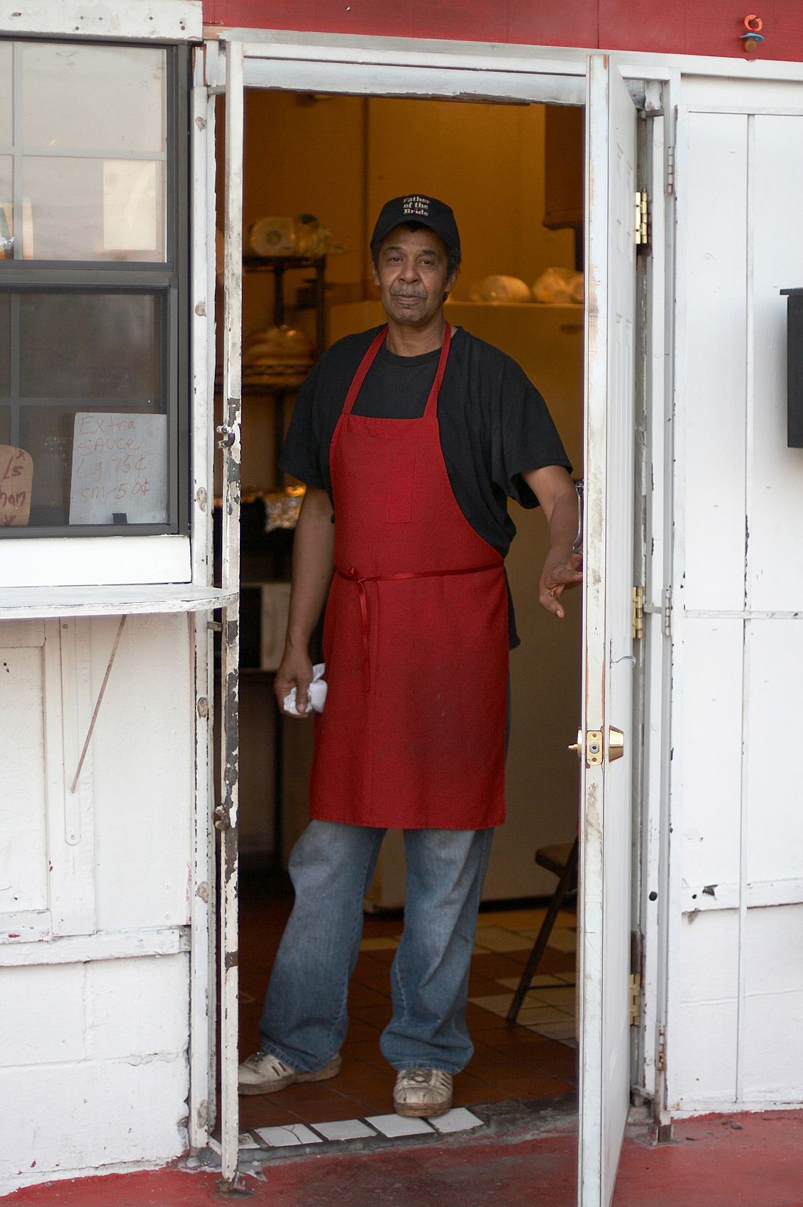 Pitmaster in a red apron standing in the open doorway of Meshack's Bar-Be-Que Shack in Garland, Texas