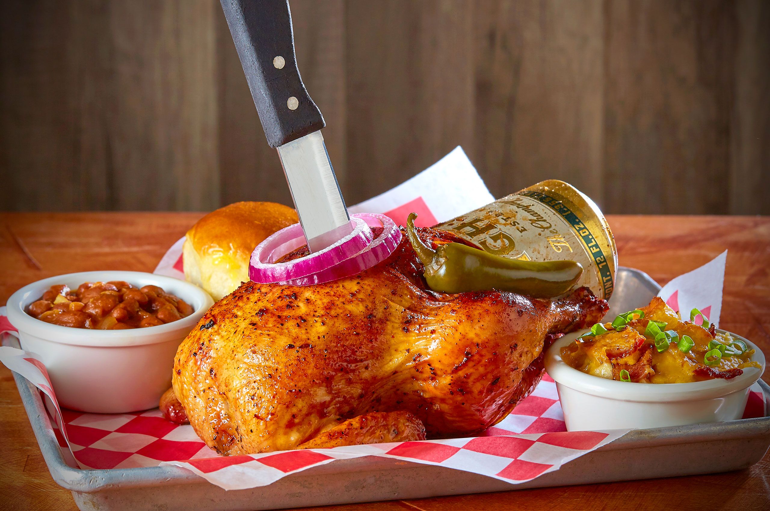 Bone Daddy's beer can chicken served in a checkered basket with baked beans, cheesy potatoes, and a roll in Dallas, Texas