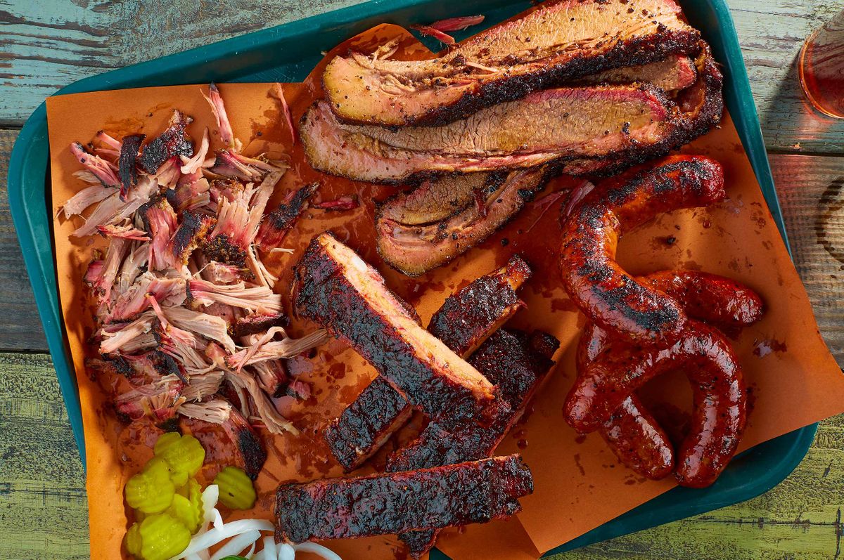 Pecan Lodge barbecue tray with brisket, pulled pork, ribs, and sausage links on butcher paper in Deep Ellum, Dallas