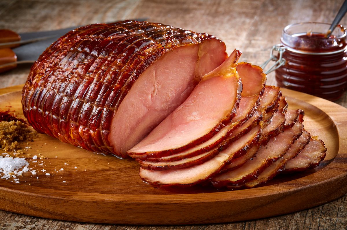 Ranch House Mesquite Smoked Meats spiral-cut glazed ham sliced on a round wood board with brown sugar, salt, and sauce