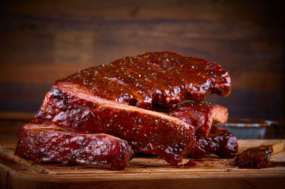 Ranch House Mesquite Smoked Meats glazed pork ribs sliced and stacked on a wood board with barbecue sauce and a basting brush