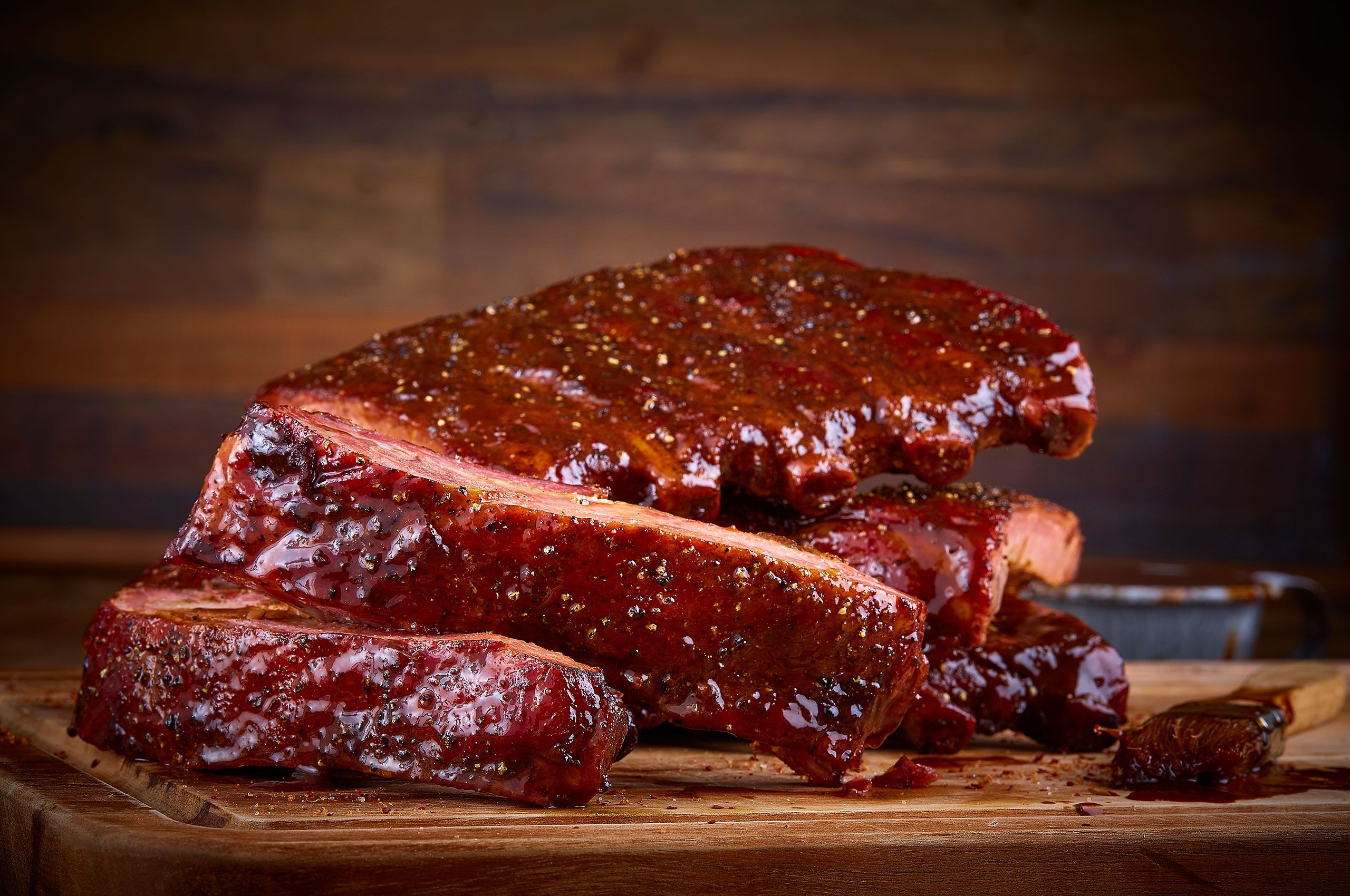 Ranch House Mesquite Smoked Meats glazed pork ribs sliced and stacked on a wood board with barbecue sauce and a basting brush