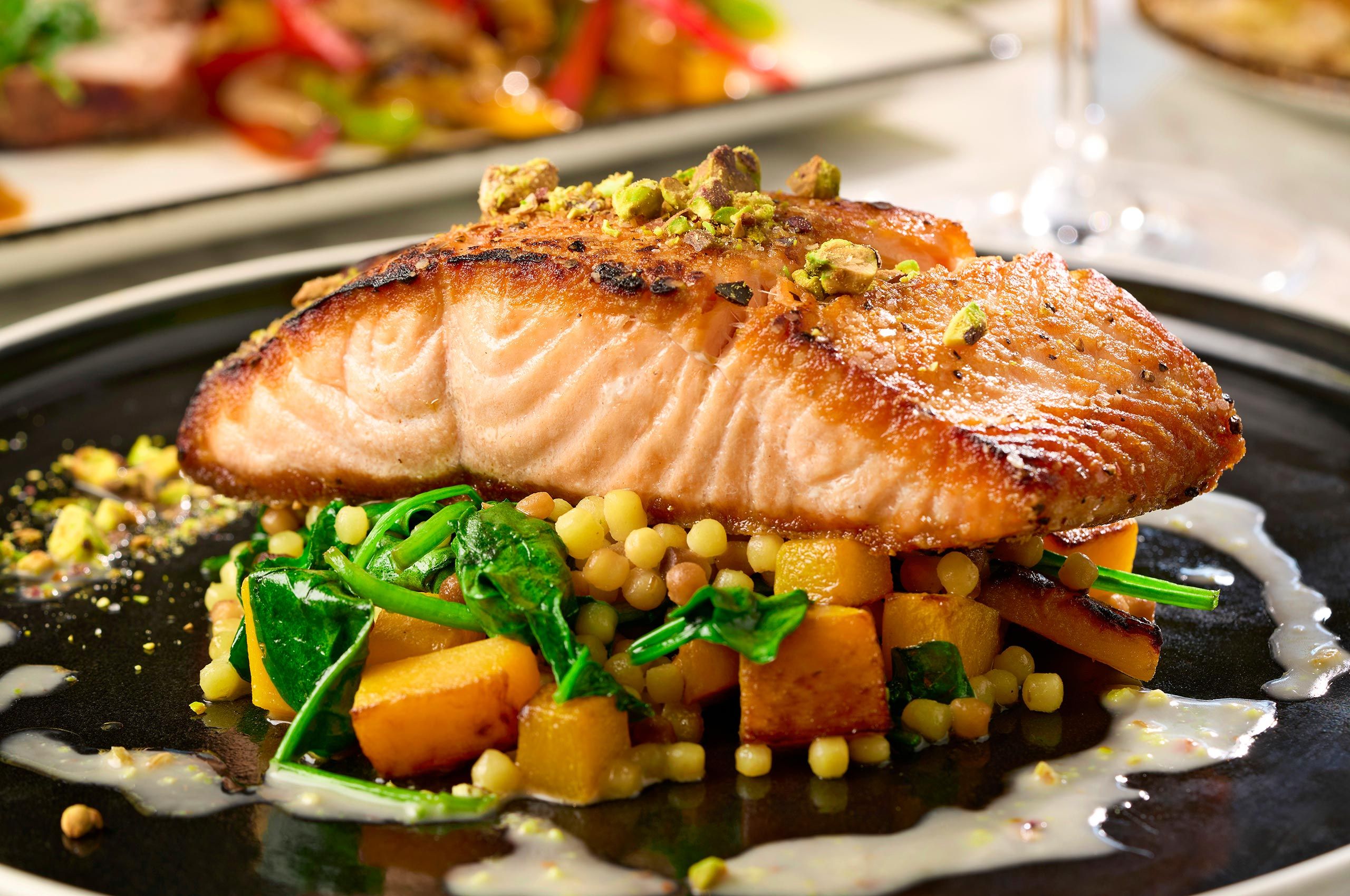 Pistachio-crusted salmon over pearl couscous, spinach, and roasted squash on a dark plate at Sauce & Vine in Fate, Texas