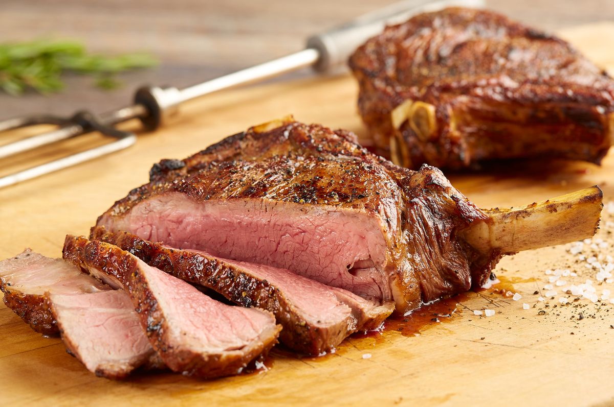 Fogo de Chão bone-in ribeye sliced on a wood board with flaked salt, cracked pepper, and a carving fork