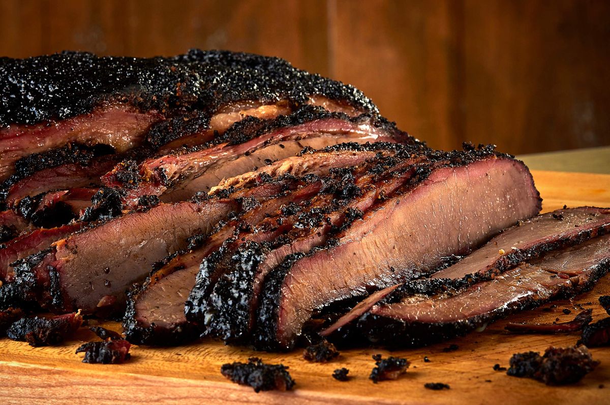 Bone Daddy's smoked brisket sliced on a wood board with a heavy peppercorn bark and visible smoke ring