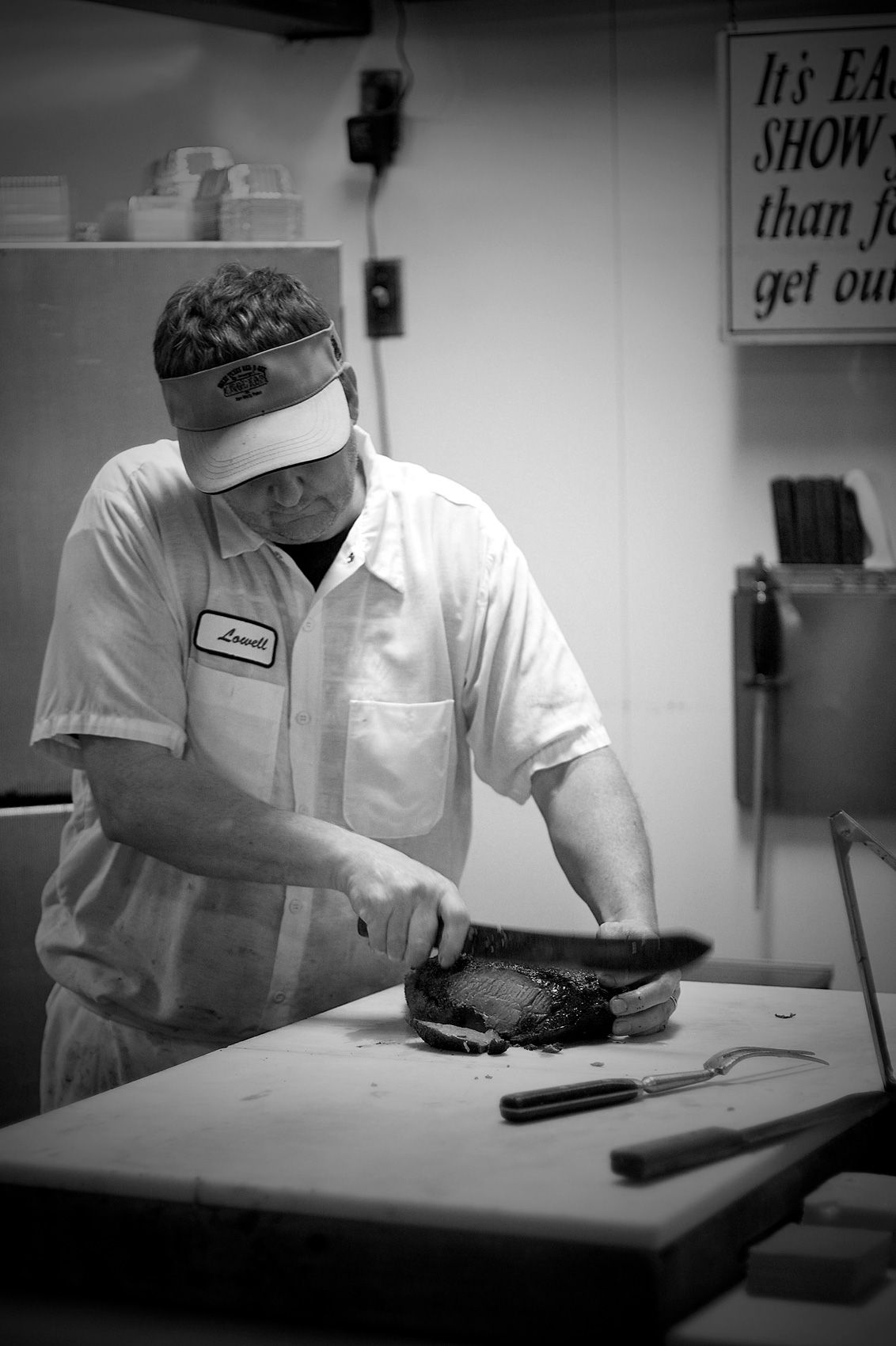 Pitmaster slicing a barked brisket with a carving knife behind the counter at Angelo's Bar-B-Que in Fort Worth