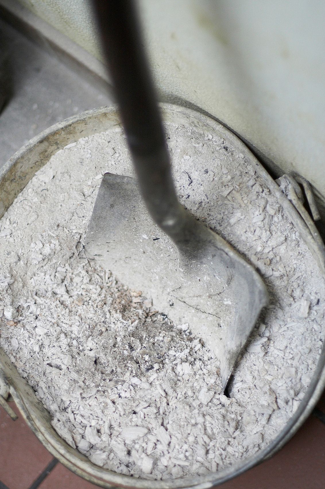 Shovel standing in a galvanized bucket of pale wood ash cleared from the pits at Smokey John's in Dallas, Texas
