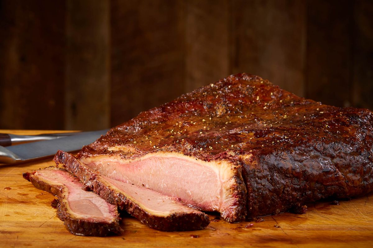 Ranch House Mesquite Smoked Meats sliced smoked brisket on a worn wood board with a carving knife