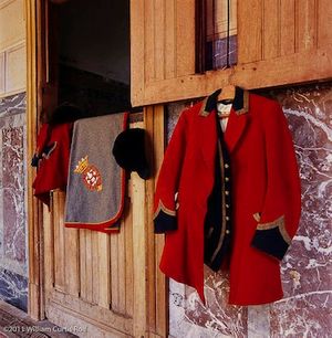 Fine-art color photograph by William Curtis Rolf capturing traditional French equestrian attire, including a scarlet red wool hunt coat and a gray saddle pad with an embroidered coat of arms at Château de Prye, France. Château de Prye France Ancestral Equestrian Attire Fine Art Color Print