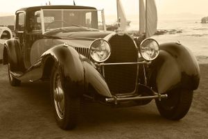 Fine-art sepia tone photograph by William Curtis Rolf capturing a rear-to-front side profile view of a dark vintage Bugatti standing against the ocean coastline at Pebble Beach. Pebble Beach Bugatti Oceanfront Profile Sepia Fine Art Print