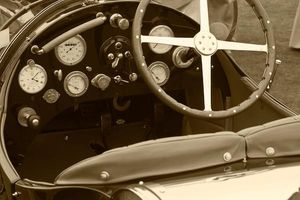 Fine-art sepia tone interior photograph by William Curtis Rolf capturing a close-up dashboard study of a classic pre-war car featuring white enamel dials and brass switches. Pebble Beach Vintage Car Dashboard White Enamel Dials Sepia Print