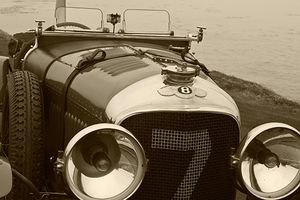 Fine-art sepia tone photograph by William Curtis Rolf capturing a front profile view of a vintage Bugatti racing car numbered 7 with large polished headlight casings at Pebble Beach. Pebble Beach Bugatti Racing Car Number 7 Sepia Print