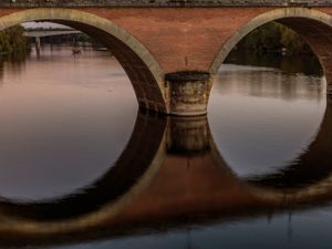 Fine‑art photograph by William Curtis Rolf showing the historic 19th‑century Bergerac Bridge in Bergerac, France. The image features the bridge’s stone‑arch construction and its exact mirrored reflection in the Dordogne River, emphasizing architectural symmetry and regional engineering significance. William Curtis Rolf fine‑art photograph of the Bergerac Bridge over the Dordogne River with symmetrical arch reflections, 19th‑century stone bridge in Bergerac, France.