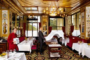 Color photograph of a waiter snapping a tablecloth and a busboy in red inside the historic Le Grand Vefour restaurant in Paris by William Curtis Rolf. Le Grand Vefour Paris Waiter Busboy Color Print William Curtis Rolf