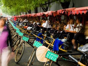 2013 color photograph of a row of bicycle rickshaws with red umbrellas and green signs waiting on a street in Beijing by William Curtis Rolf. Study 3. Beijing Rickshaw Row Red Green Color Street Print