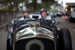 Fine-art black and white photograph by William Curtis Rolf capturing a close-up focus on a moving vintage Bentley radiator and winged B emblem with blurred drivers in the background. Pebble Beach Bentley Winged B Emblem Fine Art Black and White Print