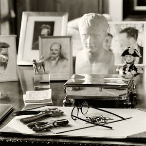 Fine-art black and white photograph by William Curtis Rolf focusing on the objects on Winston Churchill's desk inside Chartwell in Kent, England, featuring his reading glasses, personal photographs, and a bust of Napoleon under natural window light. Chartwell Kent England Winston Churchill Desk Artifacts Fine Art Print