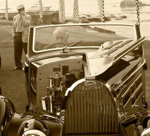 Fine-art sepia tone photograph by William Curtis Rolf capturing a vintage Bugatti with its engine compartment exposed and the driver sitting behind the wheel on the fairway at Pebble Beach. Pebble Beach Bugatti Exposed Engine Driver Sepia Print