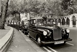 Fine-art black and white architectural photograph by William Curtis Rolf capturing vintage black taxicabs driving along the Strand with historic stone architecture in London, England. London England Taxi in the Strand 1997 Fine Art Black and White Print