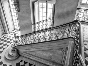 Black‑and‑white architectural study of a Versailles staircase featuring elegant wrought‑iron railing and classical stone geometry by William Curtis Rolf.