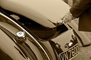 Fine-art sepia tone photograph by William Curtis Rolf capturing the polished rear tail, trunk compartment, and porcelain Bentley emblem of a vintage car at the Pebble Beach Concours d'Elegance. Pebble Beach Vintage Bentley Trunk and Emblem Sepia Print
