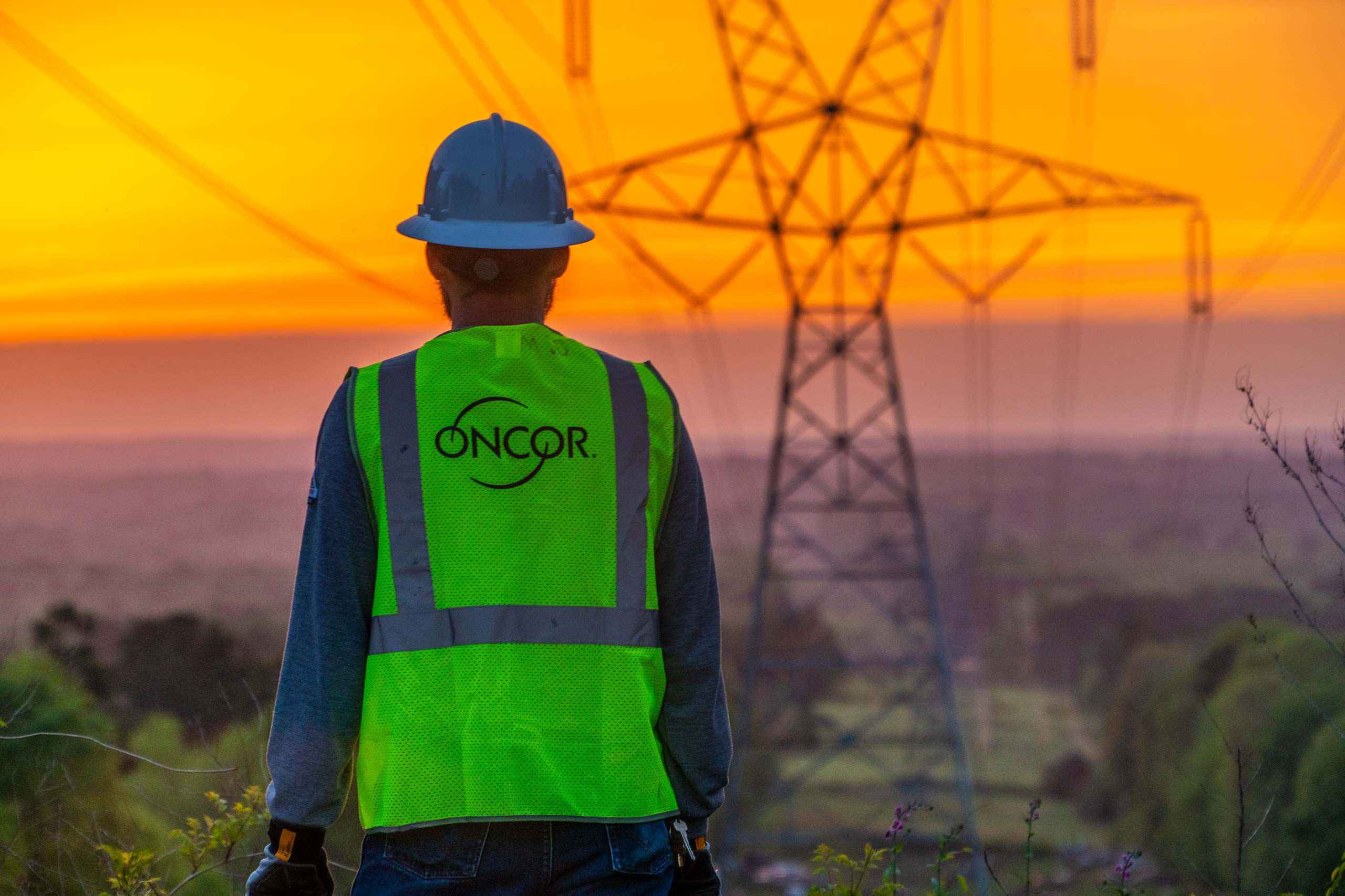 Industrial photo of an Oncor lineman observing the sunrise over a power grid, symbolizing dedication and energy infrastructure. Oncor Lineman at Sunrise Over Power Grid