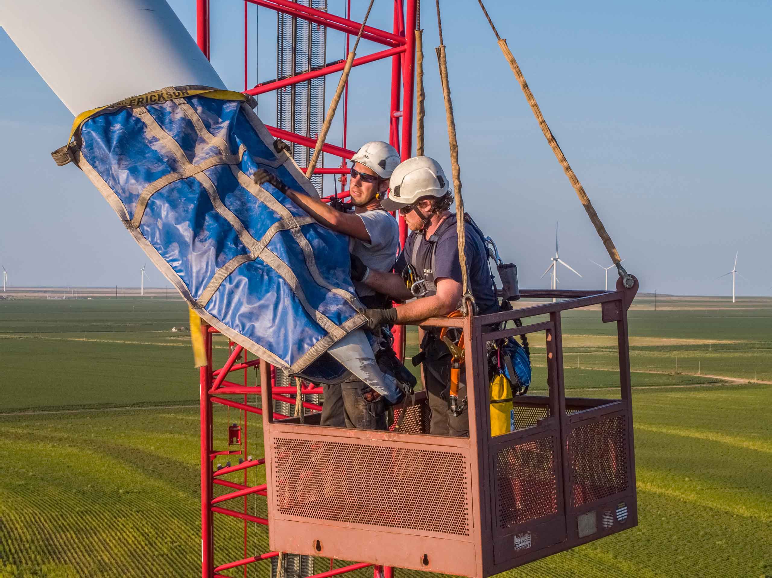 Drone aerial photo of a wind turbine technician securing the blades before removal, emphasizing safety and maintenance in renewable energy operations. Wind Turbine Technician Securing Blades - Drone Aerial View