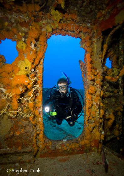 Female scuba diver shines underwater light through doorway on the shipwreck of the USCG Duane, Key Largo, Florida