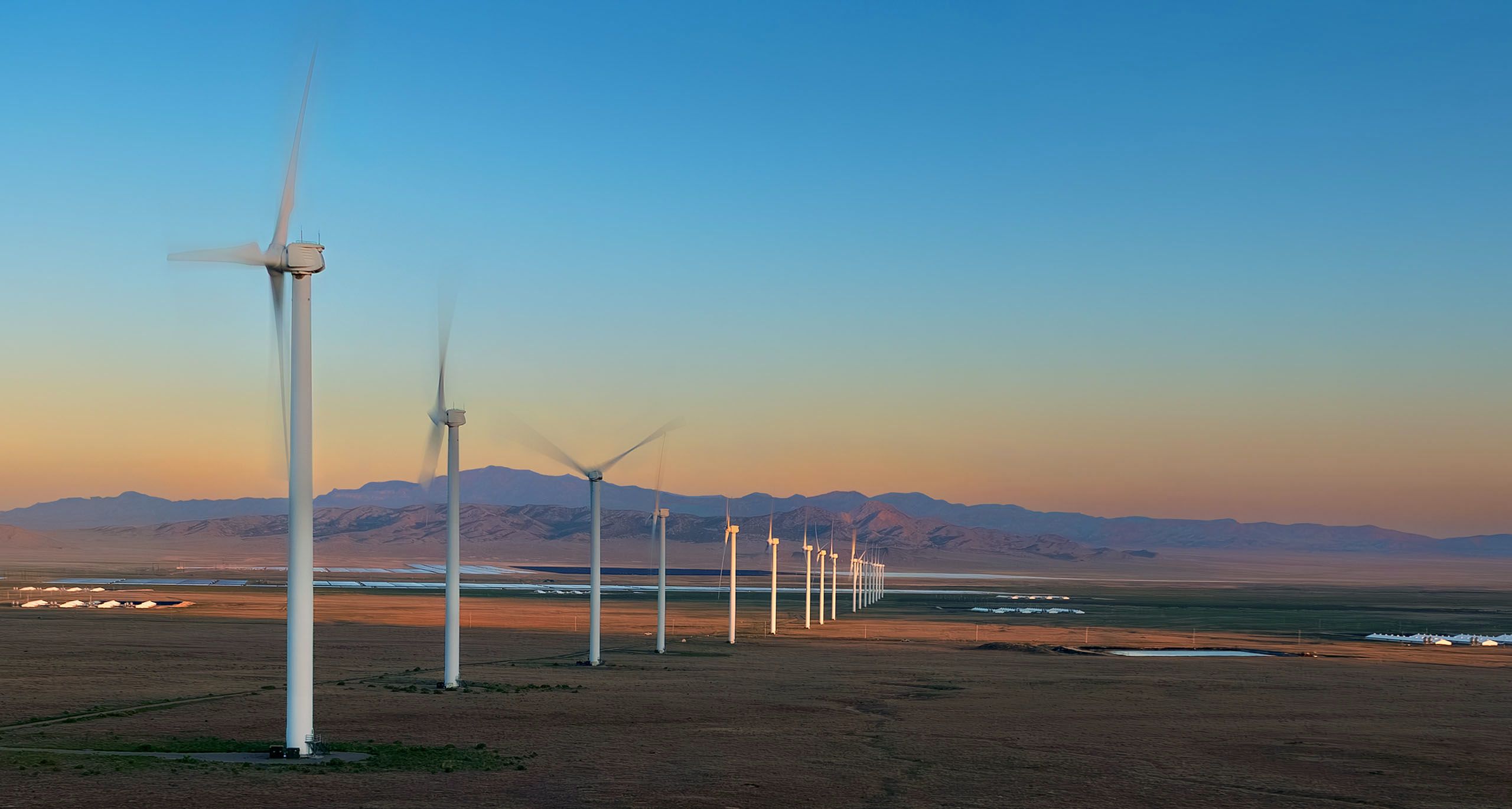 Commercial photographers out of Denver Colorado, had several photoshoots in the Milford valley in southwest Utah. This aerial drone image in warm dusk light depicts a row of wind turbines operated by Longroad Energy. Commercial Photographer - Wind Farm Under Wildfire Smoke Sky- Utah