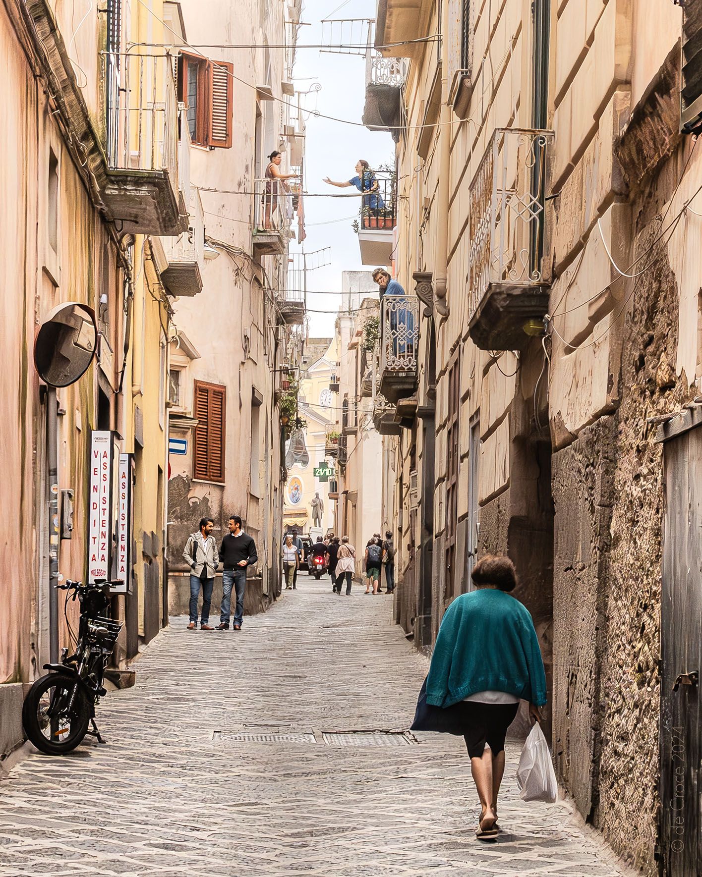 Street life in capri Italy depicts two women conversing across their balconies, another woman daydreaming in her balcony, two men walking and a woman waling from the market. Street Life Capri Italy