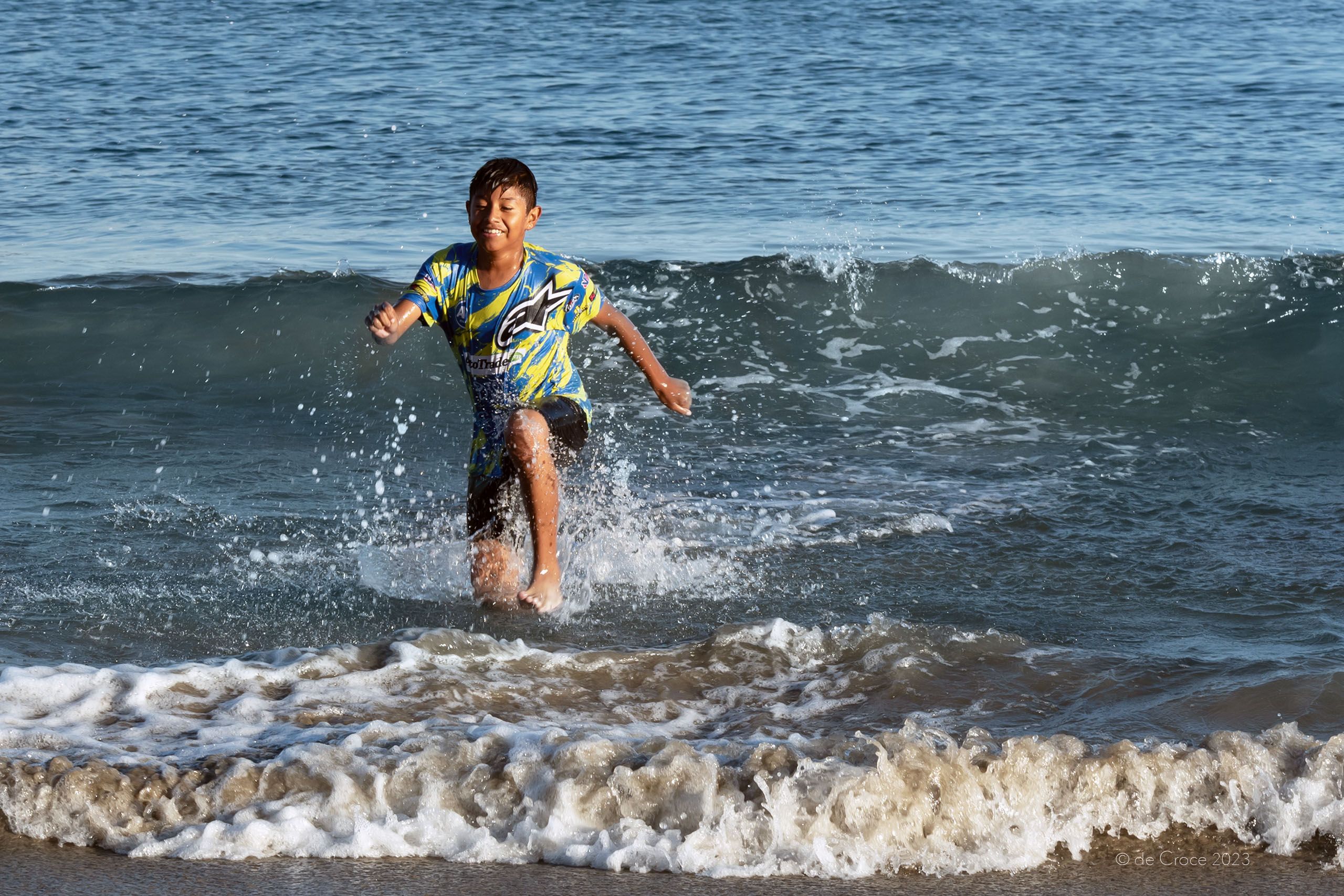 Travel photography depicting a young teenage boy running in ocean wave on Mexico beach. Boy In Wave Mexico