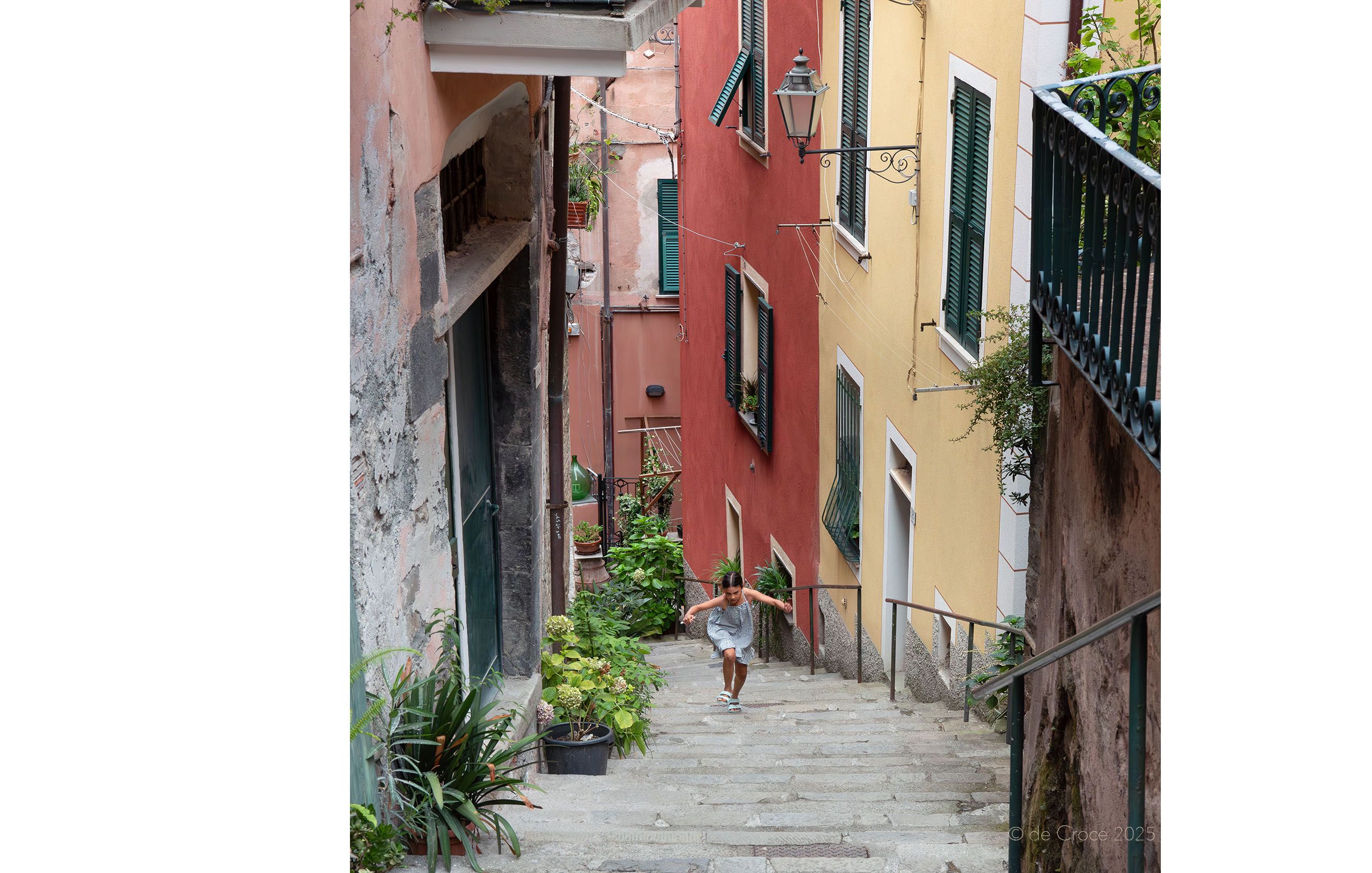 Tuscaby travel photography depicts a young girl jumping up steep steps between colorful homes Girl Jumping Steps Tuscany Italy