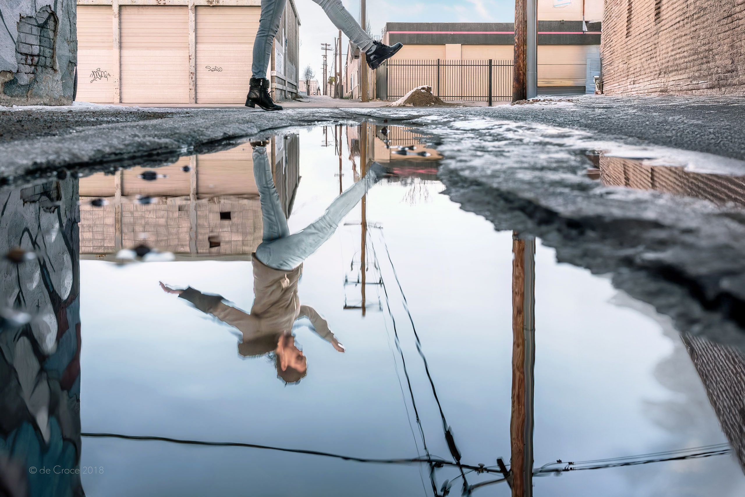 Advertisement photography for Colorado lifestyle project depicts the reflection a young woman jumping over a puddle from melting snow in Denver. Alley Ice - Colorado Lifestyle Photgraphy