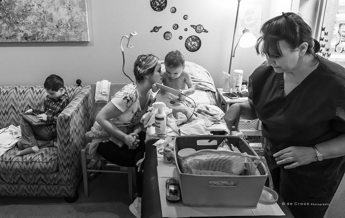 Editorial story photography of boy with EB Skin Disease and his mom, nurse and brother on family room - black and white. Family Life Photography EB Skin Disease